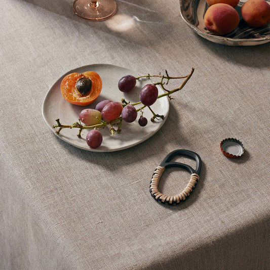 Table setting with a plate of fruit, a bowl of peaches, and decorative items on a textured tablecloth.