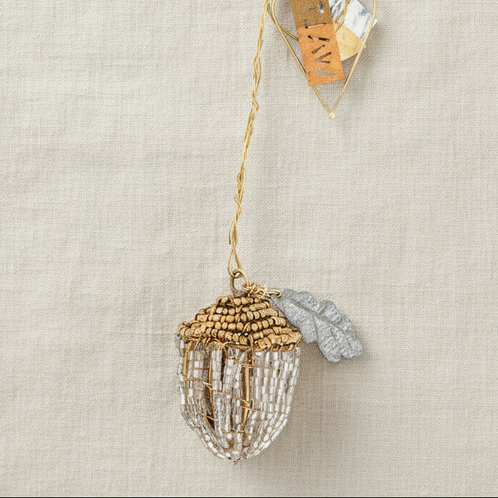 Decorative acorn ornament with clear beads and gold accents on a neutral background