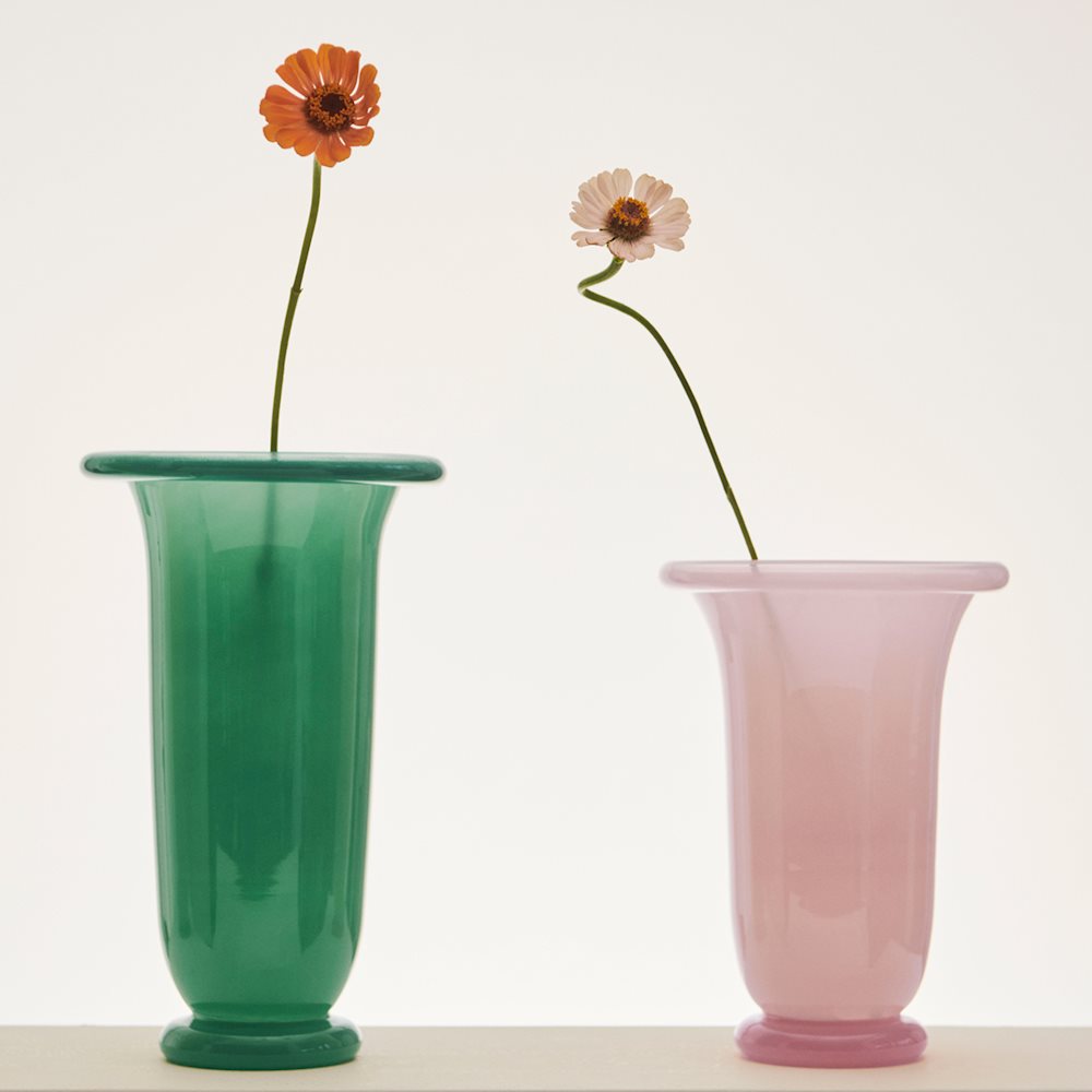Two glass vases, one green and one pink, with flowers on a white background