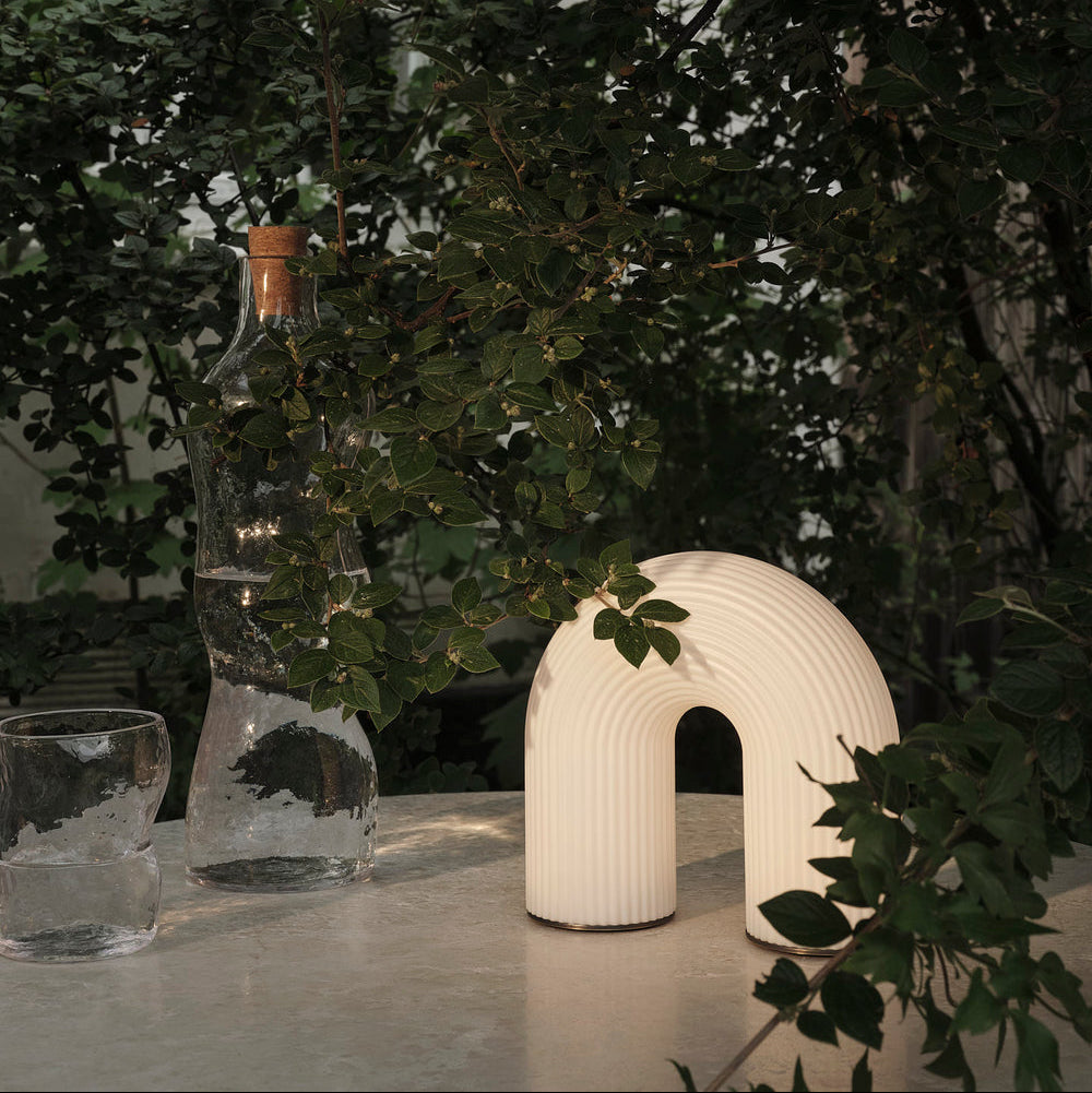 White ceramic arch-shaped lamp on a table with greenery in the background