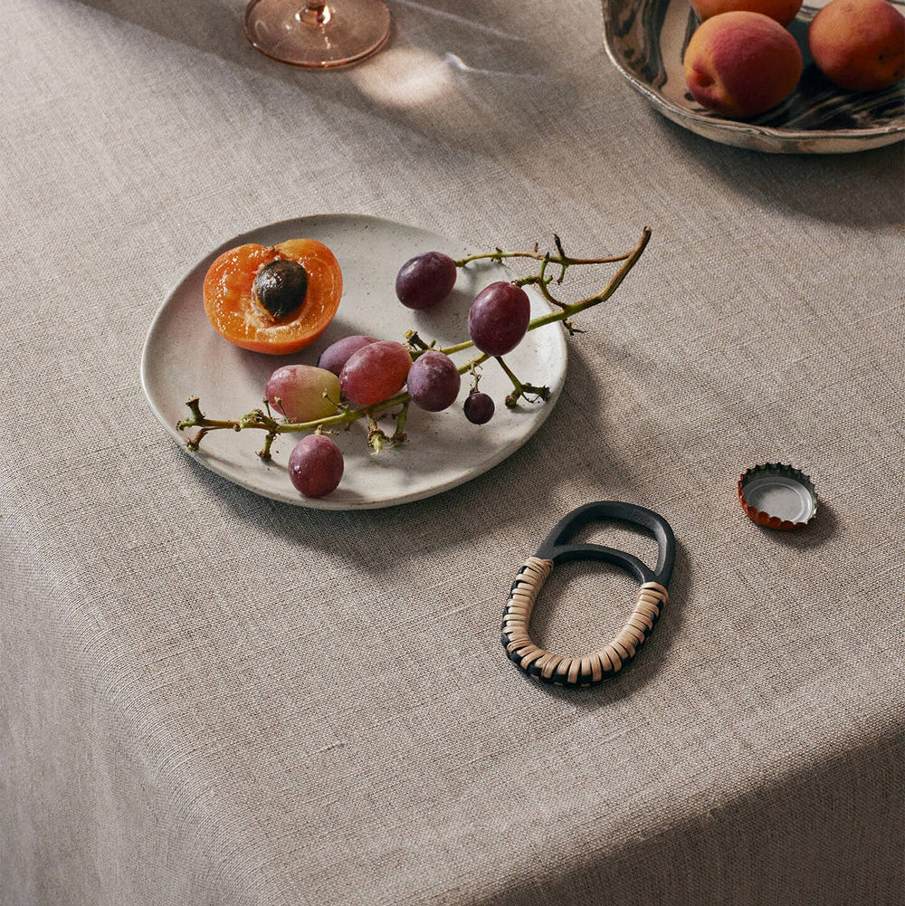 Table setting with a plate of fruit, a bowl of peaches, and decorative items on a textured tablecloth.