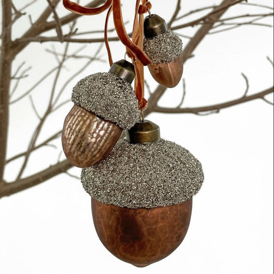 Decorative acorns with glittery caps hanging from a branch against a white background