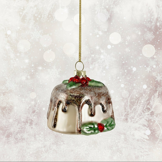 Glass Christmas ornament shaped like a bundt cake with chocolate drizzle, holly leaves, and berries on a white background.