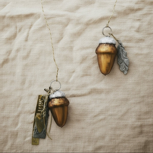 Two acorn-shaped ornaments with snow-like textures on a beige fabric background
