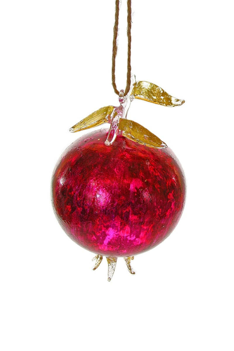 Red glass ornament shaped like a pomegranate with gold leaves on a white background
