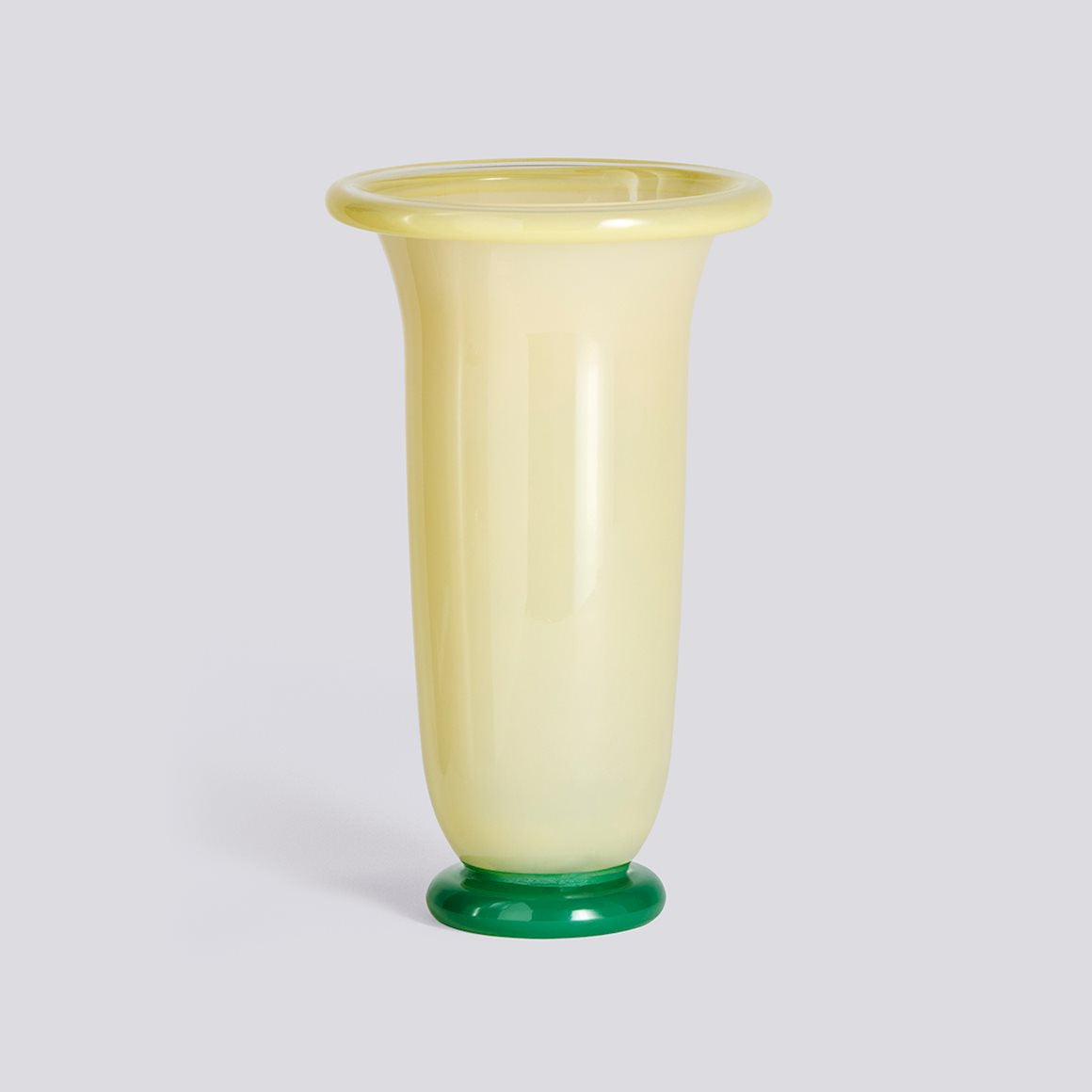 Yellow glass vase with green base on a light gray background  libertine