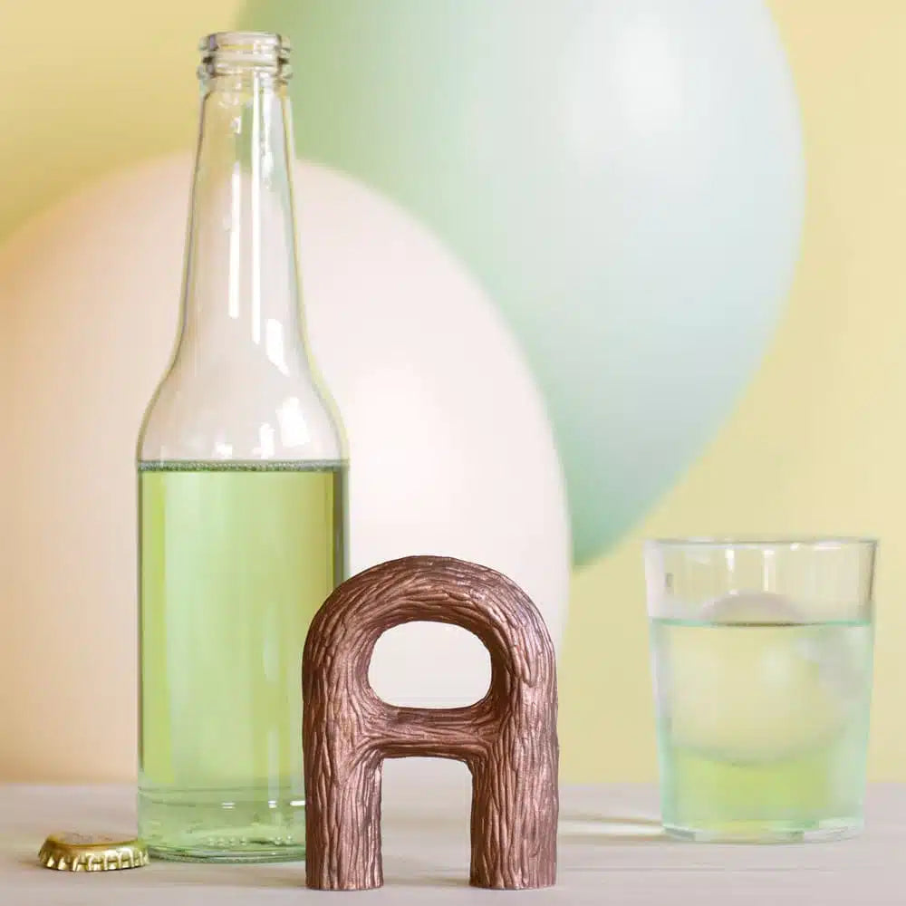 Decorative letter 'A' made of wood next to a bottle and glass with a colorful background